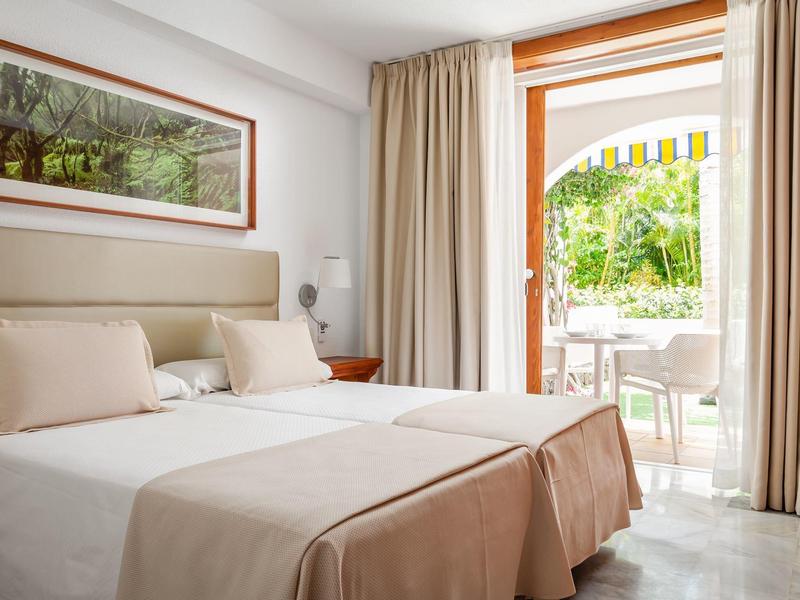 Hell eingerichtetes Schlafzimmer mit großem Bett und offener Terrassentür zum Garten.