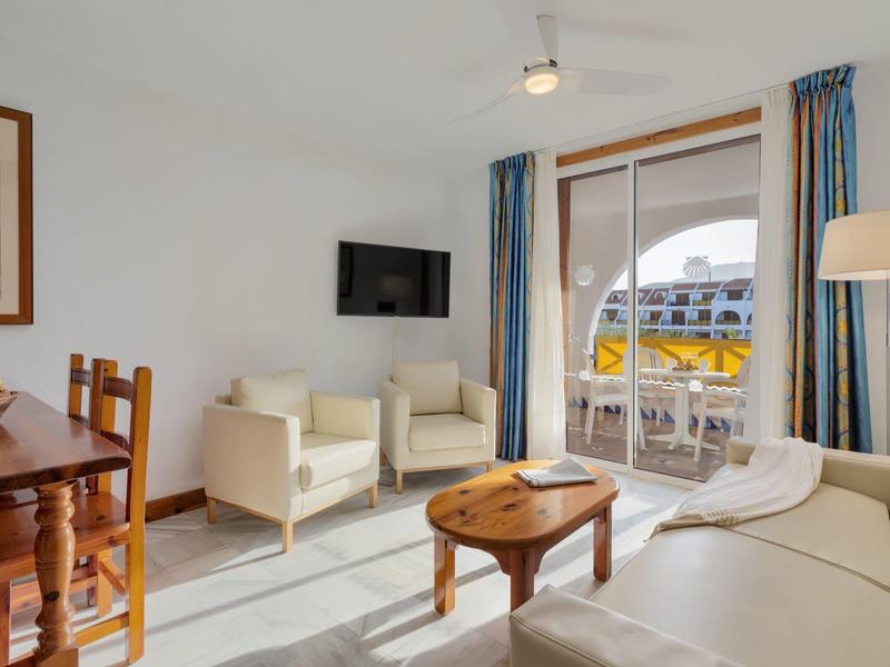 Helles Wohnzimmer mit weißen Möbeln, Holztisch, Essbereich und Balkon mit Meerblick durch Glasfenster.