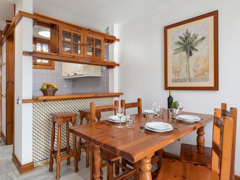 Küchen-Essbereich mit Holzmöbeln, gedecktem Tisch, Bartresen und Pflanzenbild an weißer Wand.