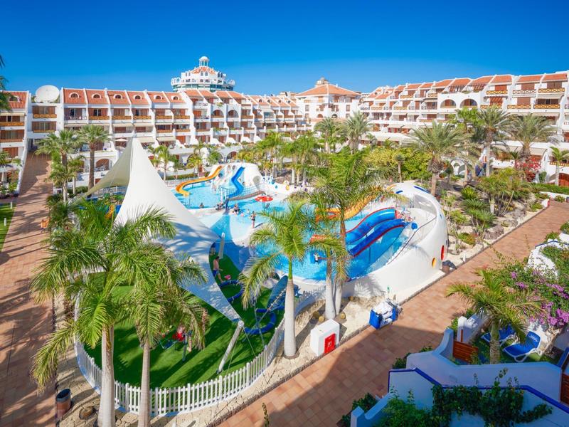 Großes Hotel mit Wasserrutschen und vielen Palmen bei klarem Himmel und sonnigem Wetter.