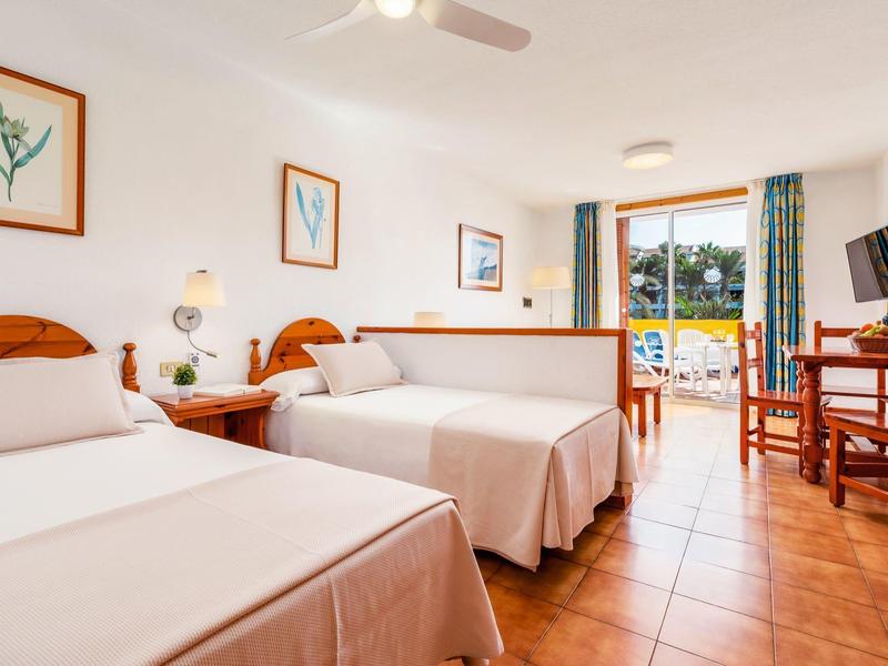 Helles Hotelzimmer mit zwei Betten, Holzmöbeln und Balkon mit Meerblick.