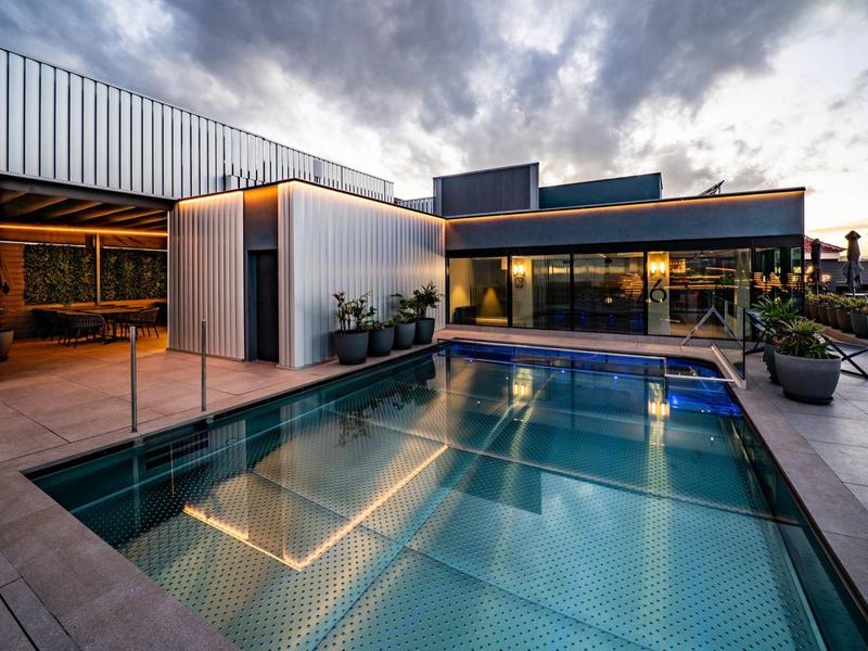 Modern pool area at sunset with glass railing and outdoor lighting.