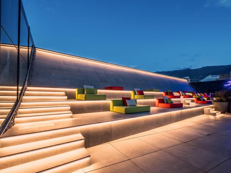 Evening view of a modern illuminated outdoor staircase with colorful cushions and mountain backdrop.