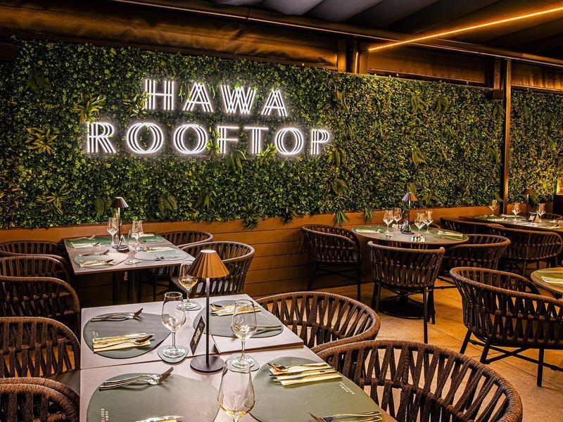 Cozy rooftop bar with green plant wall logo and stylish seating arrangements.
