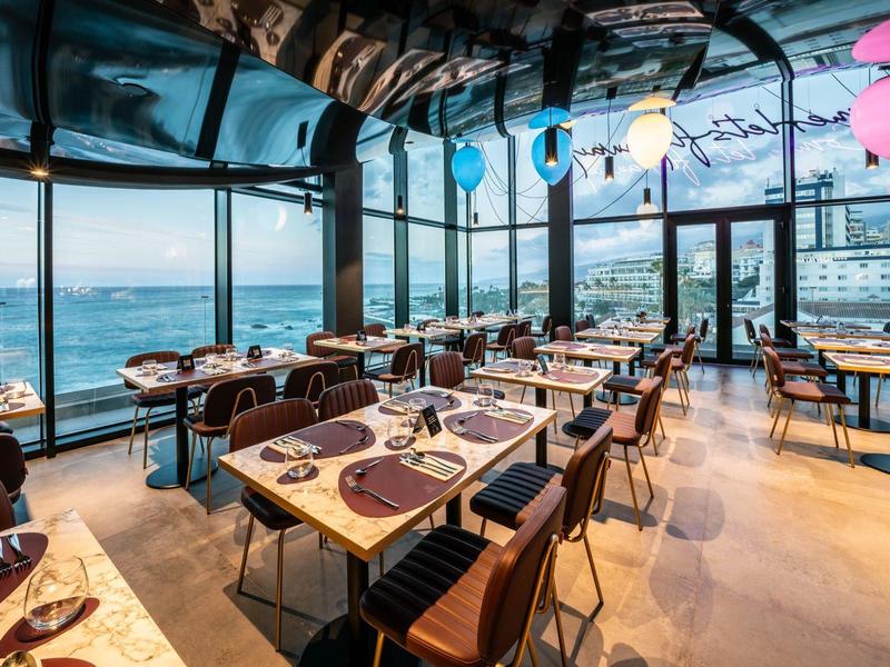 Modern restaurant with large windows and sea view, elegant tables and chairs.