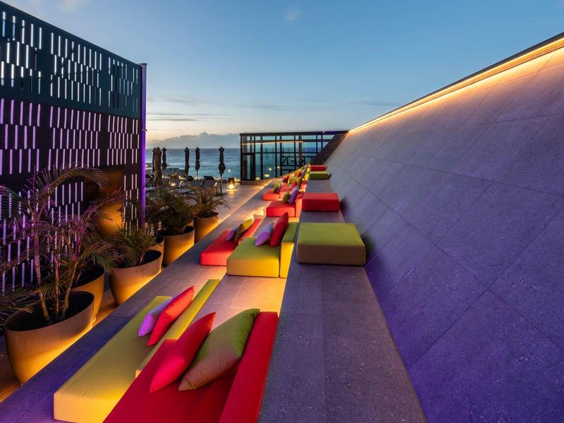 Modern rooftop terrace with cushions and sea view at sunset.