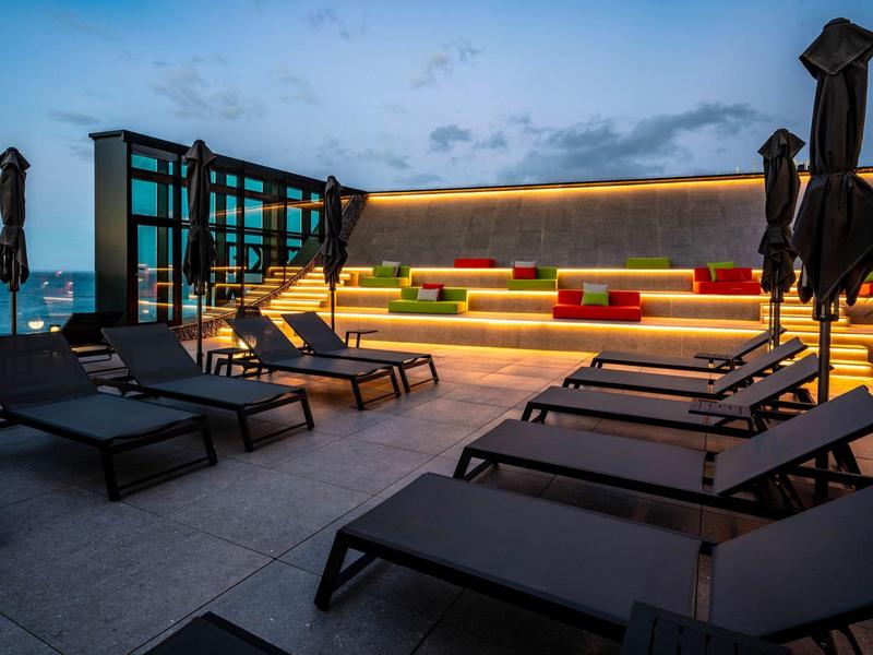 Modern rooftop terrace with seating and lounge chairs at dusk with sea view.