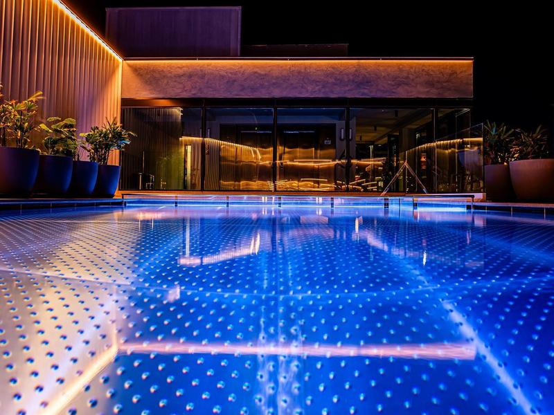 Illuminated pool at modern accommodation at night with plants and glass railing.
