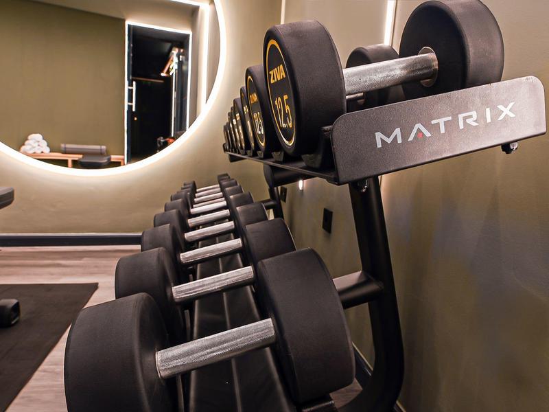Modern dumbbells stacked in a well-lit gym with a large mirror.