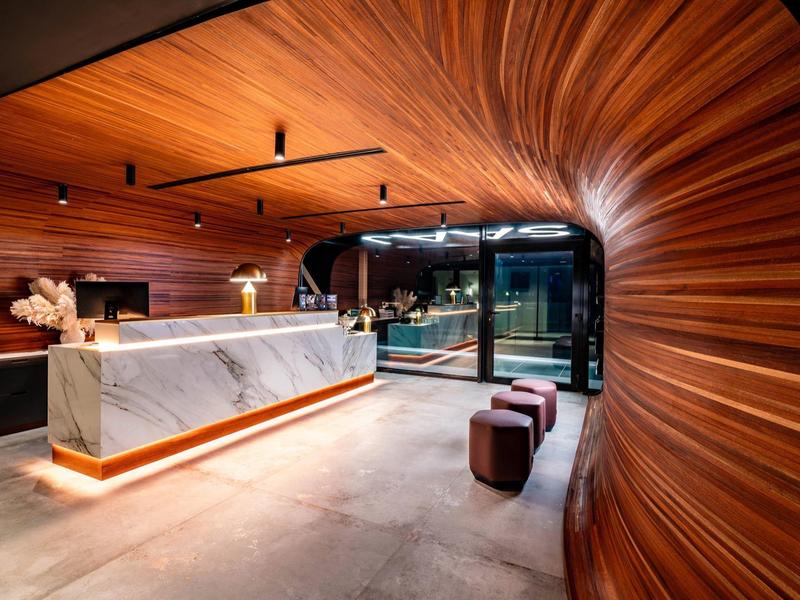 Modern hotel lobby with curved wood paneling and marble reception desk.