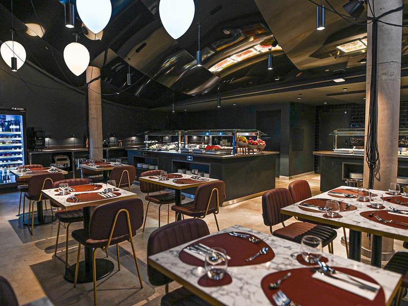 Modern hotel restaurant with set tables and open kitchen under a curved ceiling.