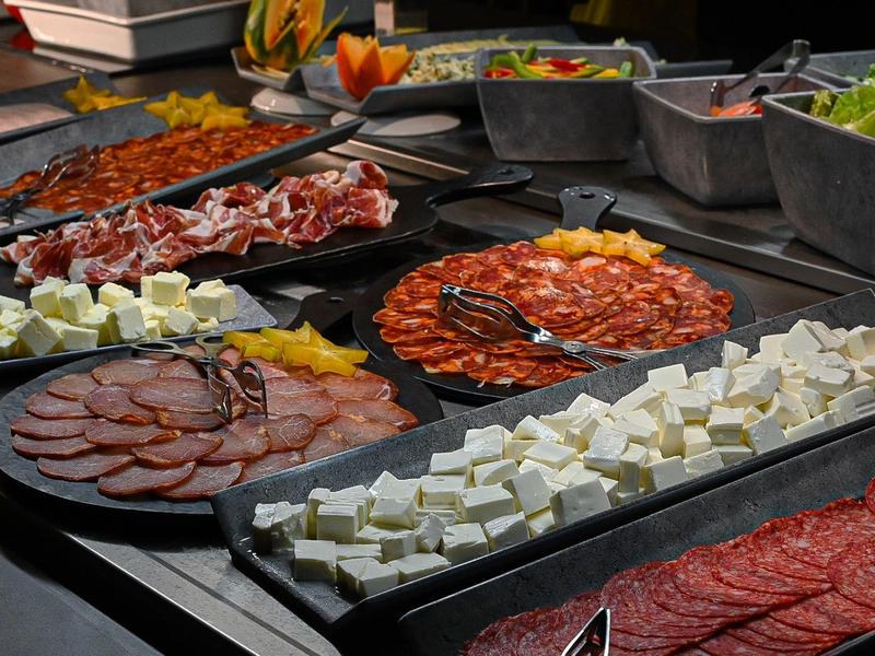 Various cold cuts and cheese varieties on a buffet with salads in the background.