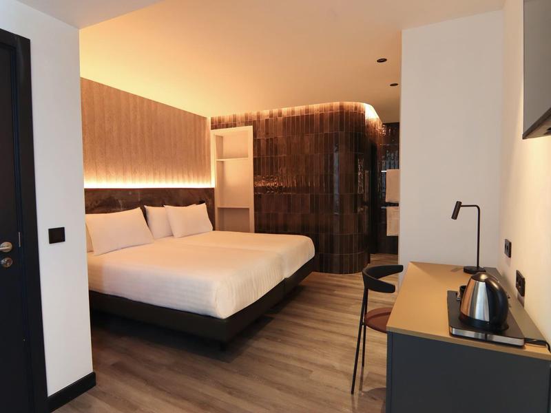 Modern hotel room with double bed, wood paneling, and a workspace with a kettle.