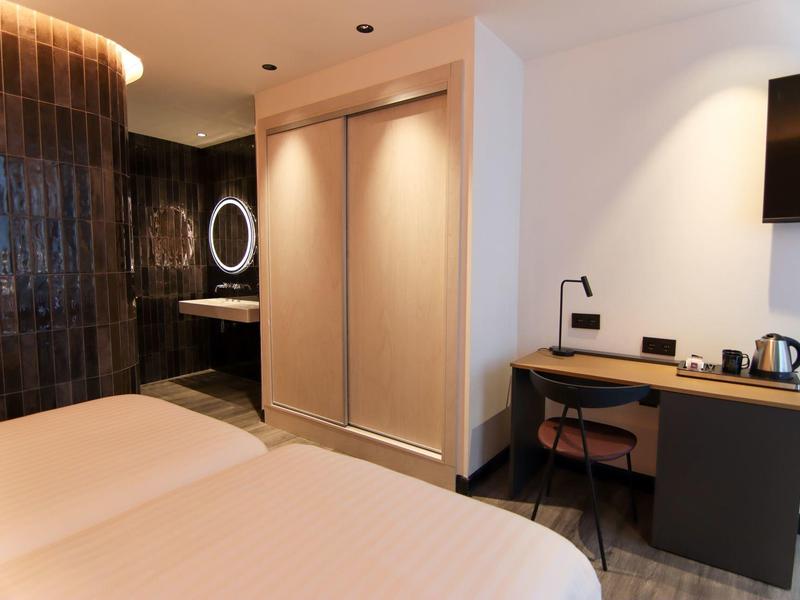 Modern hotel room with two beds, desk, and illuminated bathroom area.