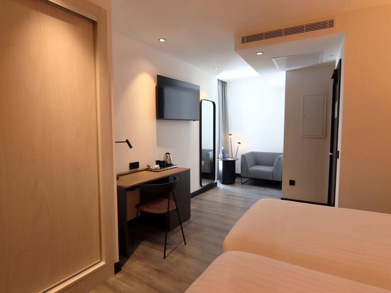 Modern hotel room with two beds, desk, and seating area.