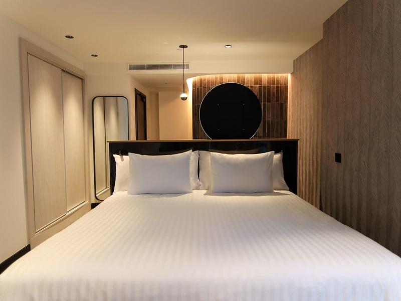 Modern hotel room with large bed, white pillows, and warm lighting.
