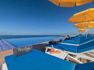 Modrá lehátka se žlutými slunečníky vedle nekonečného bazénu pod jasnou oblohou.