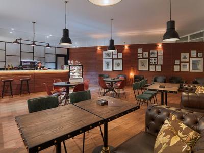 Příjemná hotelová lounge s dřevěnými stoly, koženými pohovkami a závěsným osvětlením.