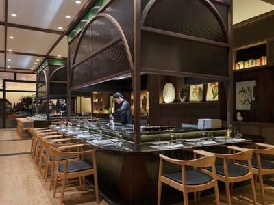 Moderní interiér restaurace s dřevěnými židlemi a bufetovým pultem pod kovovou konstrukcí.