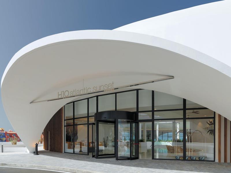 Moderní zakřivený bílý vstup do hotelu se skleněnými dveřmi pod jasnou oblohou