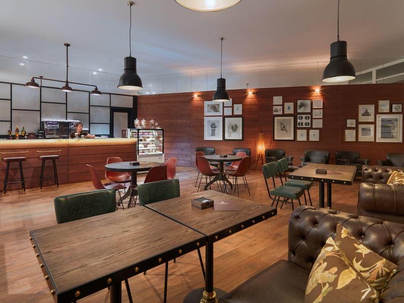 Příjemná hotelová lounge s dřevěnými stoly, koženými pohovkami a závěsným osvětlením.