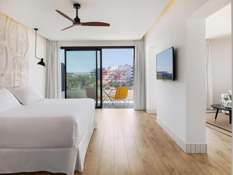 Moderní hotelový pokoj s velkou postelí, balkonem, dřevěnou podlahou a výhledem na město.