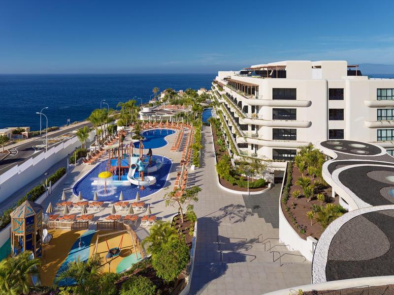 Moderní hotelový resort s venkovním bazénem a výhledem na oceán pod jasnou modrou oblohou