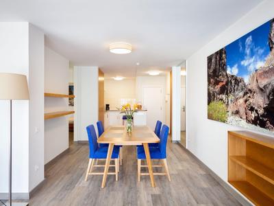 Moderní jídelní kout s modrými čalouněnými židlemi, dřevěným stolem a fotografií krajiny na zdi.