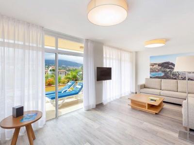 Světý obývací pokoj s pohovkou, konferenčním stolkem, televizí a přístupem na terasu s výhledem na bazén a hory.