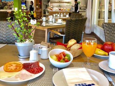 Snídaňový stůl s džusem, ovocem, rohlíky a uzeninami v moderní hotelové restauraci.