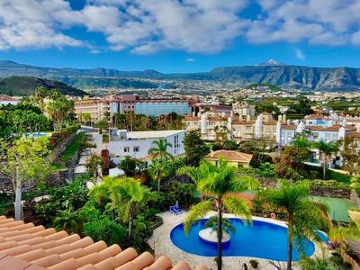 Výhled na město s bazénem, zelenými zahradami a horami pod zataženou oblohou.