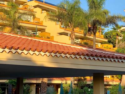 Hotelová budova s žlutou barvou, slunečními paraplemi a palmami pod modrou oblohou