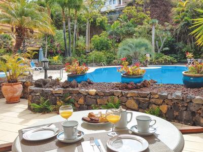 Terasa s prostřeným stolem a výhledem na tropickou zahradu s bazénem.