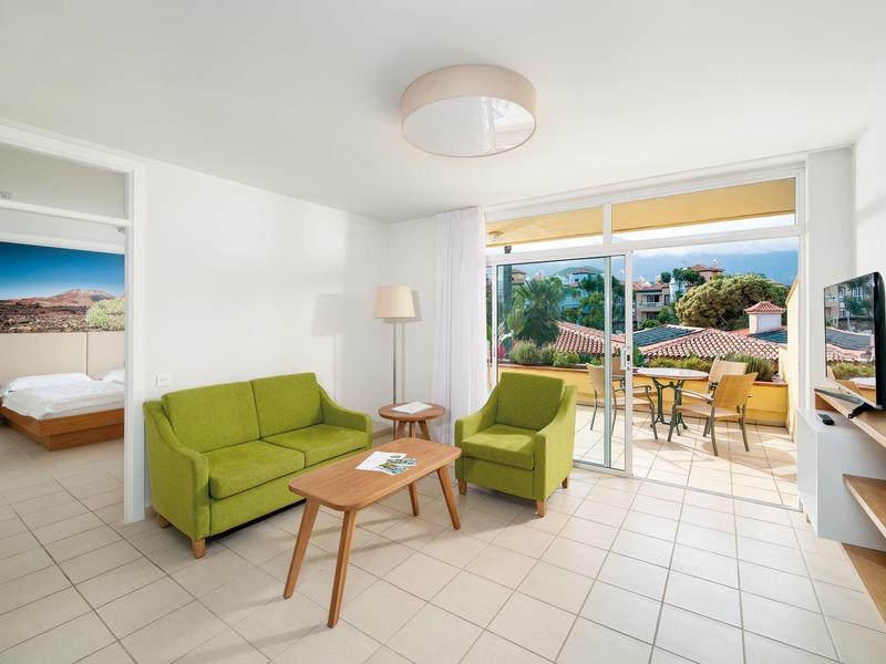 Světý obývací pokoj se zelenou pohovkou, křesly a přístupem na terasu s výhledem do zeleně.