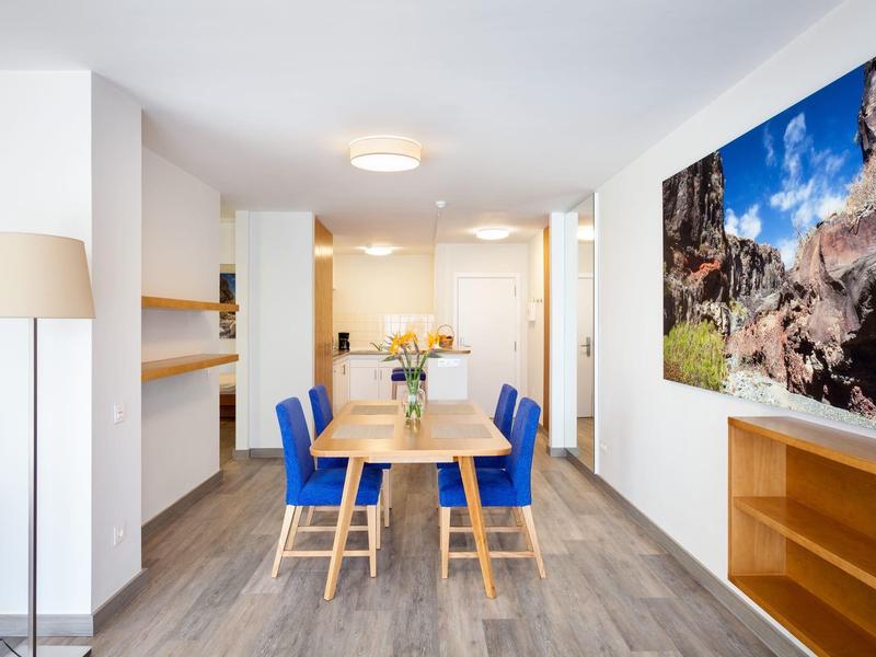 Moderní jídelna s dřevěným stolem, modrými židlemi a velkou přírodní fotografií na zdi.