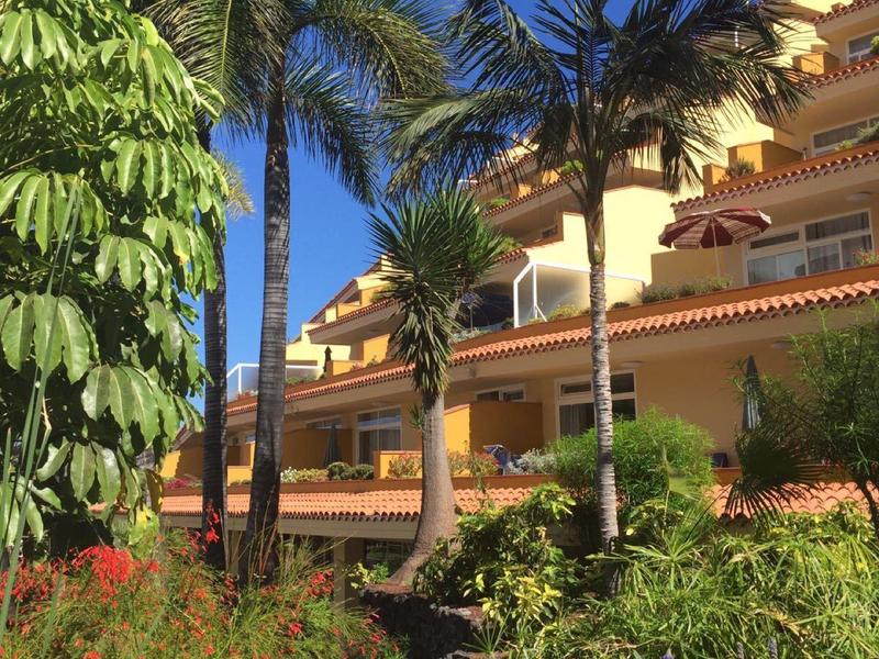 Hotel s tropickými rostlinami a palmami pod jasně modrou oblohou