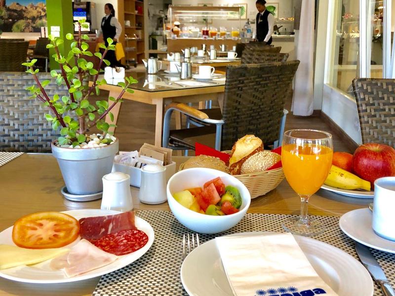 Snídaňový stůl s džusem, ovocem, rohlíky a uzeninami v moderní hotelové restauraci.