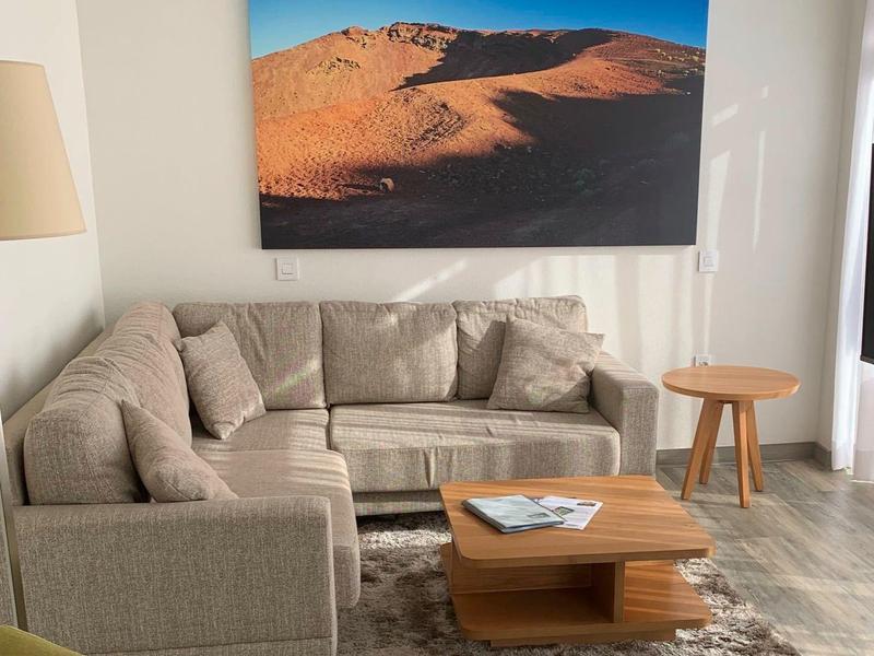 Pohodlný obývací kout se šedou rohovou pohovkou, dřevěným stolkem a krajinářským obrazem na stěně.