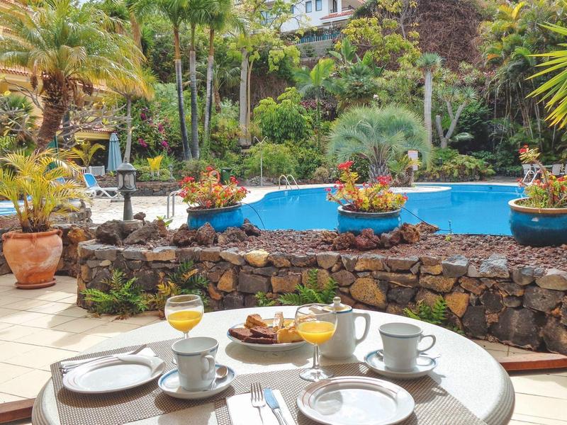 Terasa s prostřeným snídaňovým stolem, bazénem a tropickou zahradou v pozadí.