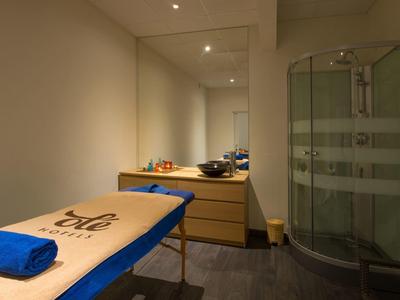 Una stanza benessere luminosa con lettino da massaggio, specchio, cassettiera e cabina doccia rotonda.