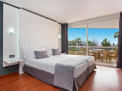 Camera d'hotel moderna con letto matrimoniale, pavimento in legno e ampia vetrata con vista sul balcone.