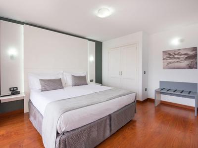 Camera d'hotel luminosa con letto matrimoniale, pavimento in legno e arredamento minimalista.