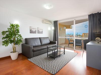 Soggiorno moderno con divano grigio, piante e accesso al balcone con vista sulla città.