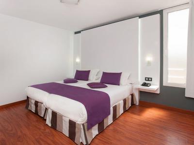 Camera moderna con letto grande, accenti viola e pavimento in legno.