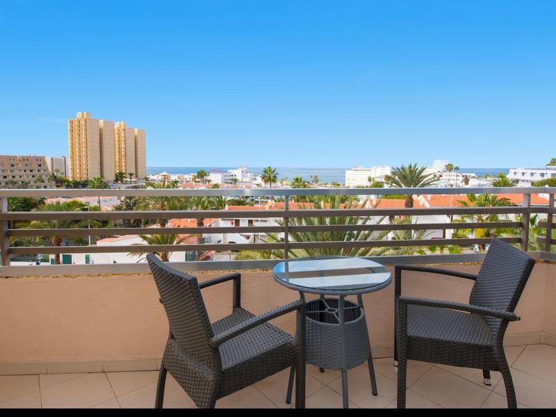 Balcone con due sedie e un piccolo tavolo con vista sulla città e cielo azzurro.