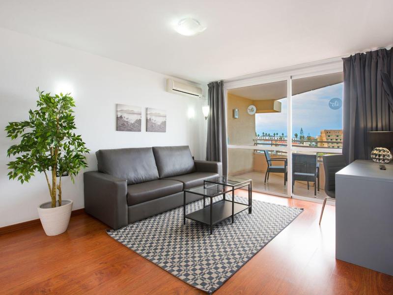 Soggiorno moderno con divano grigio, piante e accesso al balcone con vista sulla città.