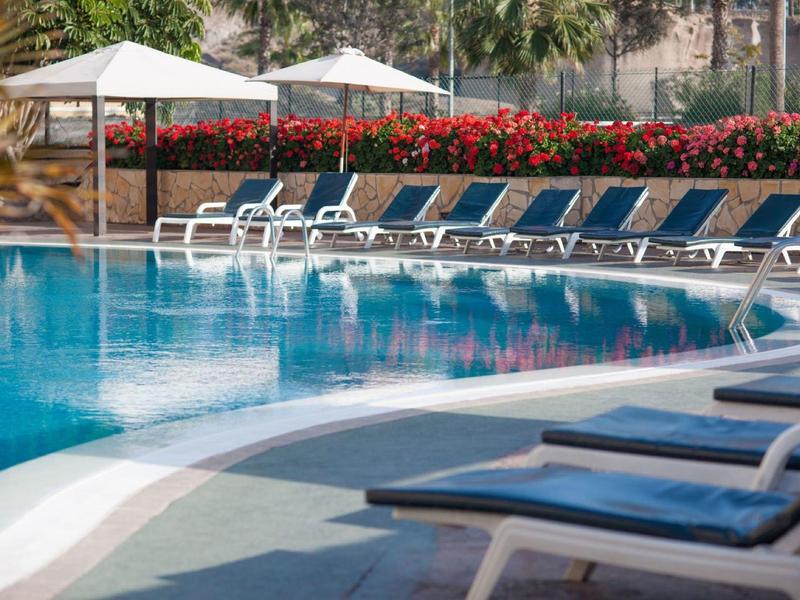 Piscina dell'hotel accogliente con lettini blu e ombrelloni, circondata da vegetazione verde.
