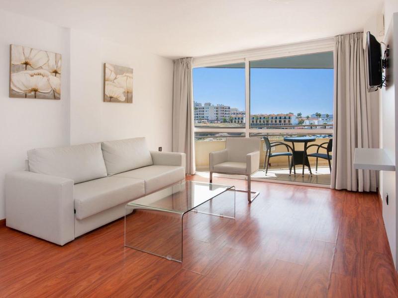 Soggiorno luminoso con divano, tavolo in vetro e balcone con vista sulla città.