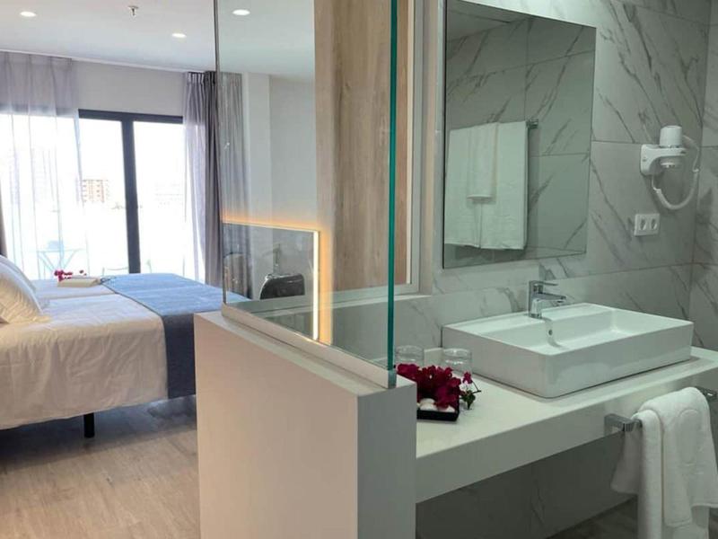 Moderne hotelkamer met open badkamer, wastafel en een bed met licht beddengoed.