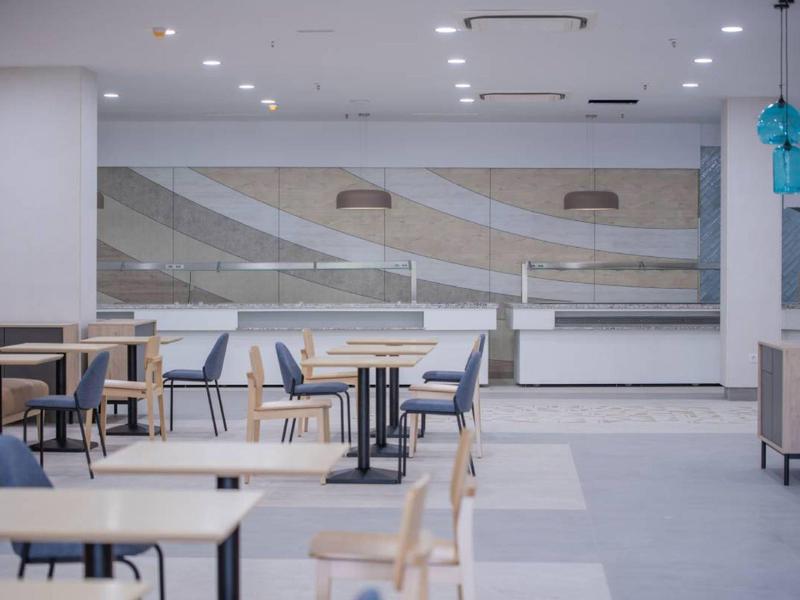 Moderne, lichte eetruimte met tafels, stoelen en plafondlampen.